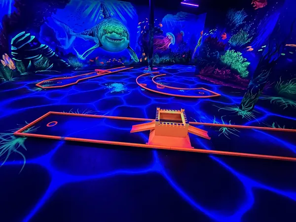 Schwarzlicht-Minigolfbahn in der Unterwasserwelt mit Hai an der Wand und leuchtenden Korallen